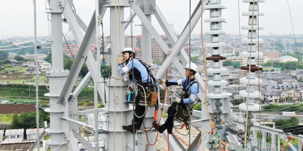 住宅地を背景に送電鉄塔で点検作業を行うラインマン