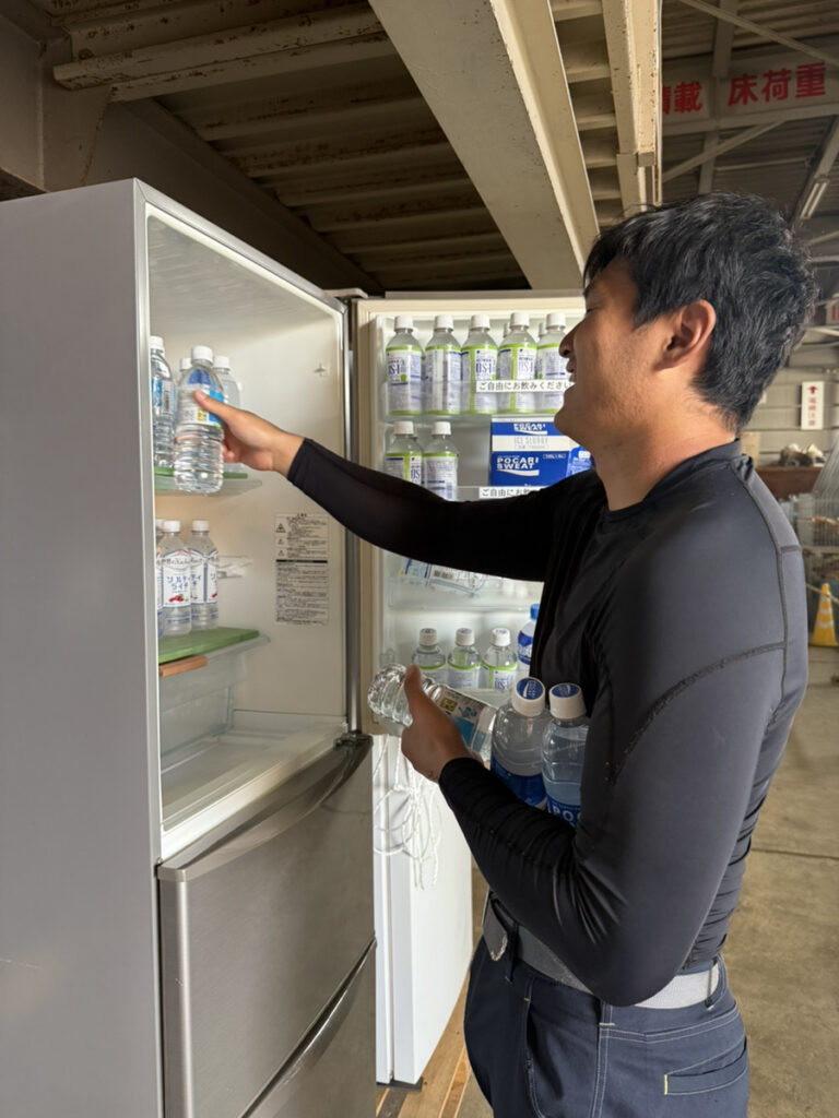 現場作業員用に熱中症対策として提供されている飲料水を取り出している男性技術者