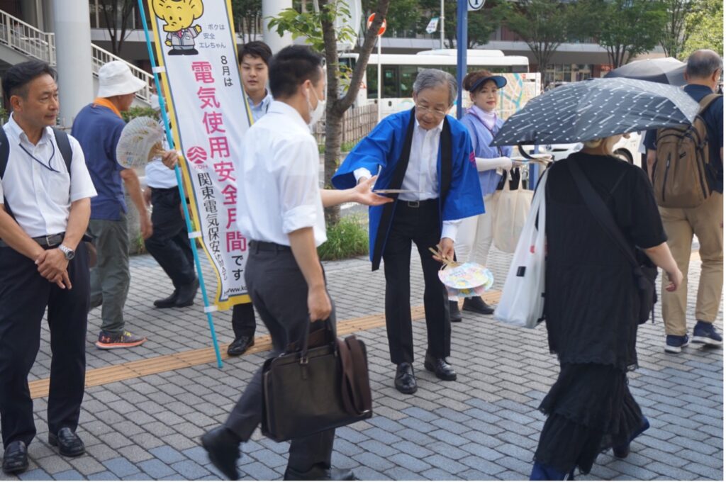 駅前でうちわを配る武部会長の様子