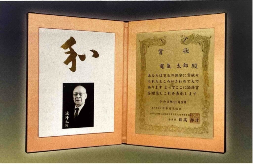 賞状見本：賞状は見開きで革張り、右の賞状部分は金属に文字が彫られている。