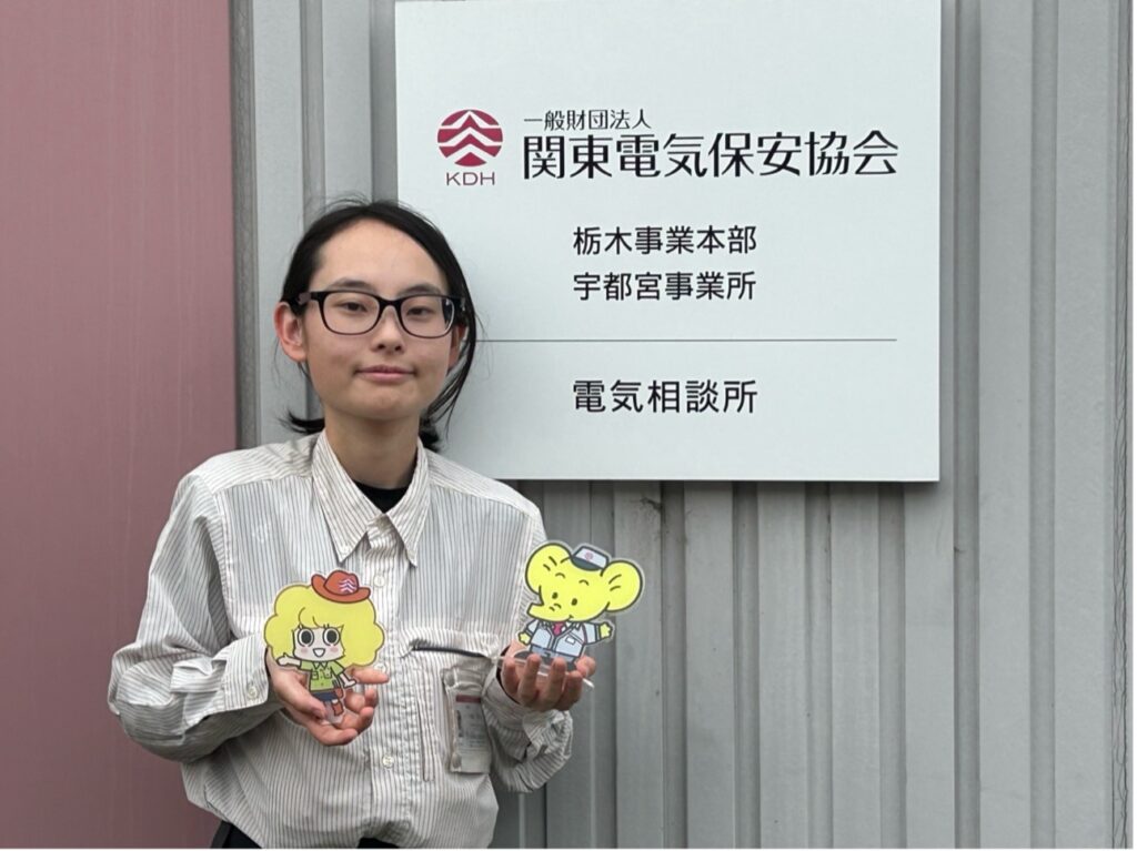 電気保安協会のキャラクターのアクスタを両手に持つ飯塚さん